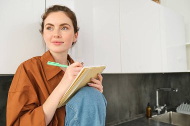 Genç yaratıcı kızın portresi, fikirlerini planlamakla, ödevlerini deftere yazmakla, mutfak tezgahında oturmakla..