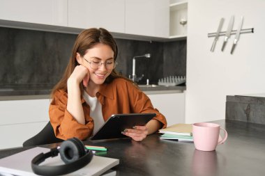 Evden çalışan genç bir kadının portresi, dijital tablet dersine bağlanmak, gözlük takmak, mutfağında uzaktan eğitim, uzaktan öğrenme ve eğitim kavramı..