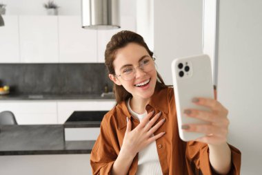 Güzel genç bir kadın, sosyal medya blogcusu video kaydı, online video sohbeti akıllı telefondan, cep telefonuyla evde duruyor..
