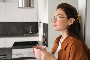 Evdeki rahat, güzel ve rahat genç kadının portresi, ayakta ve duvara yaslanmış bir fincan kahveyle, düşünceli bir yüz ifadesiyle çay içiyor..