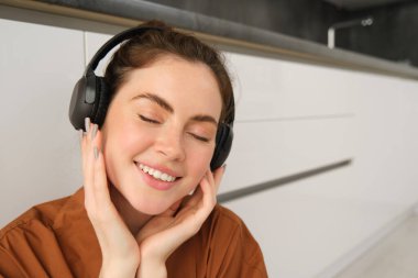 Güzel esmer kadının yakın portresi, kablosuz kulaklıkla müzik dinliyor, kafasında yeni kulaklıklar var, gülümsüyor ve mutlu görünüyor..