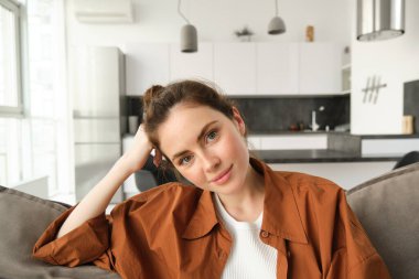 Yaşam tarzı konsepti. Genç gülümseyen esmer kadın, koltukta oturmuş, dinleniyor, rahat bir ifadeyle kameraya bakıyor..