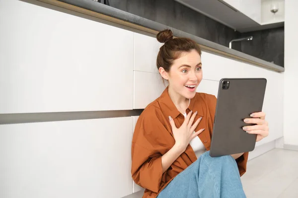 Portrait of friendly smiling woman video chats, connects to online conversation on digital tablet, says hello at camera.