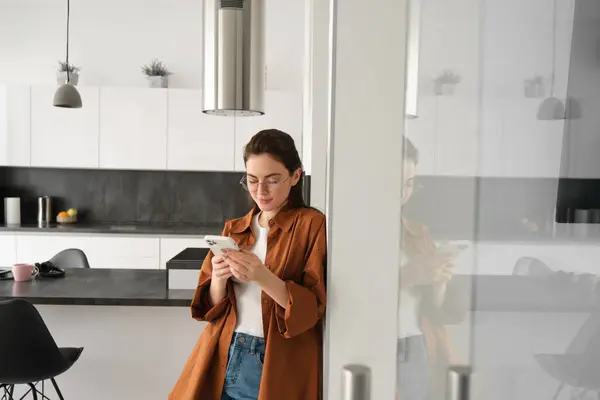 Portrait of cute young woman standing at home with smartphone, reading message on mobile phone, using application, order online, paying utility bill in app.