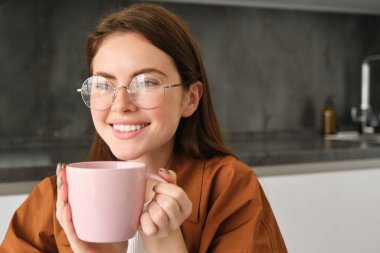 Bir fincan çayla rahatlayan mutlu bir kadının portresi. Kız kahvenin tadını çıkarıyor, gülümsüyor ve mutlu görünüyor, evinde rahat hissediyor..