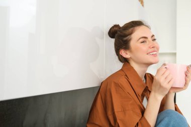 Hoş anlar. Mutlu genç kadın mutfakta oturur ve kahve içer, yüzünde şefkatli bir gülümseme vardır..