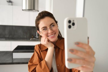 Güzel genç bir kadın, sosyal medya blogcusu video kaydı, online video sohbeti akıllı telefondan, cep telefonuyla evde duruyor..