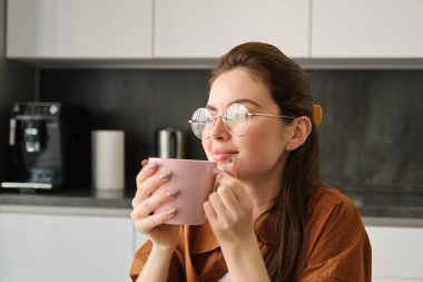 Dinlenen genç bir kadının portresi, çay içen. Kız mutfakta çay içiyor, elinde kupa tutuyor ve düşünceli görünüyor..