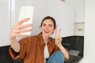 Güzel genç bir kadının portresi akıllı telefonuyla resim çekiyor, fotoğraflara poz veriyor, kendi için filtre uygulaması kullanıyor..