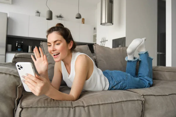 Carefree Young Smiling Woman Lying Sofa Saying Hello Waving Smartphone — Stock Photo, Image