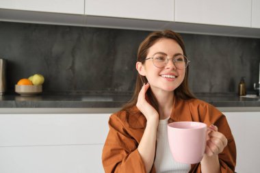 Gözlüklü güzel bir genç kadının portresi, gülümsüyor, evde dinleniyor, fincanı kahveyle tutuyor, çay içiyor..