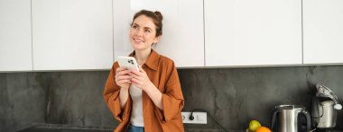 Akıllı telefonlu genç bir kadının görüntüsü, düşünceli bir ifadeyle, internetten cep telefonu uygulaması kullanarak, telefon uygulaması ile yemek siparişi veriyor..