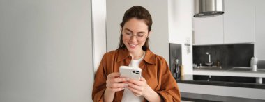Evde akıllı telefon kullanırken sosyal medyayı kontrol eden güzel bir kadın. Gülümseyen genç bir bayan cep telefonu uygulaması kullanıyor ve oyun oynuyor, online alışveriş yapıyor ya da haberleri okuyor. Boşluğu kopyala.