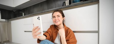 Mutlu gülümseyen kadın video sohbetlerinin portresi, mutfakta oturmuş, sosyal medya uygulamasında akıllı telefon kullanarak arkadaşınla konuşuyor..