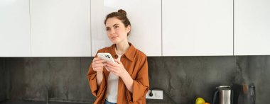 Akıllı telefonlu genç bir kadının görüntüsü, düşünceli bir ifadeyle, internetten cep telefonu uygulaması kullanarak, telefon uygulaması ile yemek siparişi veriyor..