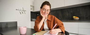 Güzel genç bir kadın, evde çalışan serbest çalışan bir kız, mutfakta oturuyor ve yazıyor. Ödev yapan, ders çalışan kız öğrenci..