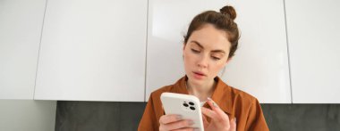 Akıllı telefonuna düşünceli bir yüzle bakan, internetten alışveriş yapan, mobil uygulama kullanarak internetten bir şeyler alan bir kadının portresini kapat..