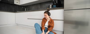 Evdeki mutfak zemininde sevimli modern kız, kablosuz kulaklıkla müzik dinliyor, eğleniyor..