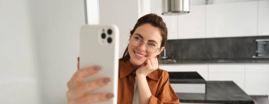 Güzel genç bir kadın, sosyal medya blogcusu video kaydı, online video sohbeti akıllı telefondan, cep telefonuyla evde duruyor..