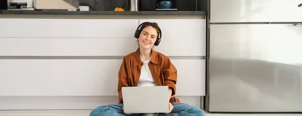 stock image Portrait of young beautiful woman in headphones, sits on floor with laptop, works from home, student does her homework on computer, listens to music.