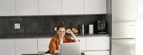 Portrait of woman freelancer, programmer working from home. Female student or business owner sitting with laptop in kitchen.