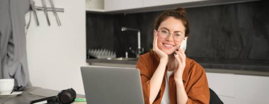 Serbest çalışan genç bir kadının portresi, evden çalışan bir girişimci, serbest çalışan bir müşterinin. Sipariş veren, telefonla konuşan, mutfakta dizüstü bilgisayarla oturan bir kız..