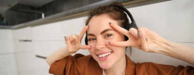 Kaygısız genç bayanı kapat, gülümse, huzur göster, v-işareti yap, kablosuz kulaklıkla müzik dinle..