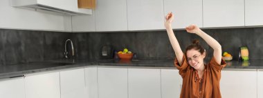 Gülümseyen, gözlüklü, uzaktan kumandayla çalışan, bilgisayarla çevrimiçi ders çalışan, mutlu bir şekilde ellerini uzatan genç bir kadının dikey görüntüsü..