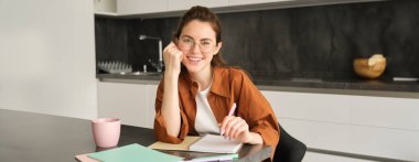 Gülümseyen genç bir kadının portresi, özel öğretmen evde ders notları hazırlıyor, deftere yazıyor ve mutlu görünüyor, mutfakta okuyan bir öğrenci..