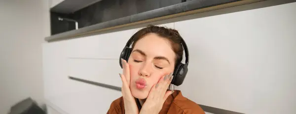 stock image Beautiful young woman in wireless headphones, makes silly and cute faces, listens to music at home.