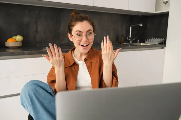 Portrait of surprised, happy woman in glasses, looking at laptop with amazed, excited face expression, positive reaction to big news.