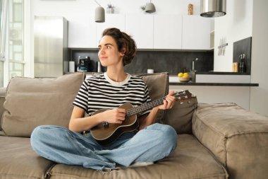 Oturma odasında dinlenen, ukulele çalan bir kızın portresi, yeni bir müzik aleti çalmayı, evde dinlenmeyi öğreniyor..