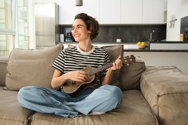 Oturma odasında dinlenen, ukulele çalan bir kızın portresi, yeni bir müzik aleti çalmayı, evde dinlenmeyi öğreniyor..