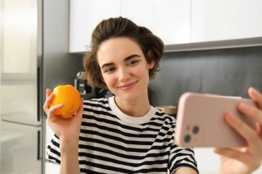 Gülümseyen, güzel genç bir kadın taze sarı biberle selfie çekiyor, yemek blogcusu mutfakta sebzelerle selfie çekiyor, vegan sosyal medya için yemek yapıyor ve video kaydediyor..