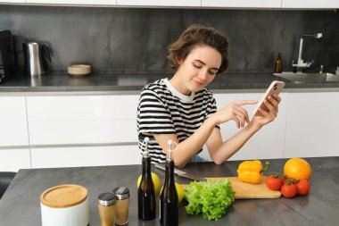 Mutfakta güzel esmer kadın portresi, yemek pişirme, akıllı telefon tarifi arama, yemek blogu için fotoğraf çekme, sebzelerden yemek pişirme, vejetaryen salatası..
