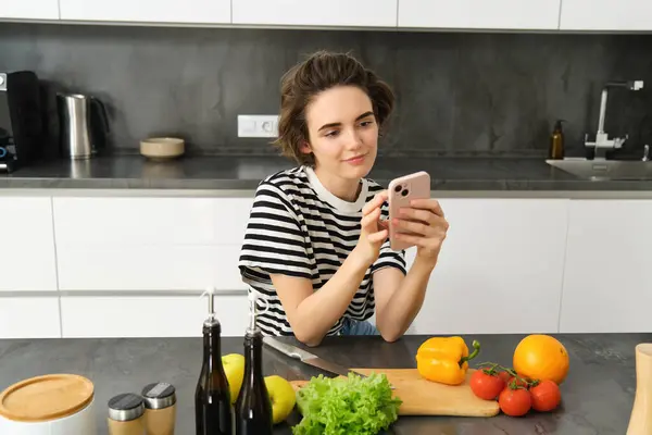 Mutfakta güzel esmer kadın portresi, yemek pişirme, akıllı telefon tarifi arama, yemek blogu için fotoğraf çekme, sebzelerden yemek pişirme, vejetaryen salatası..
