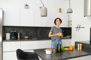 Mutlu, sağlıklı genç bir kadının portresi, vejetaryen salata yapıyor, sebzelerin yanında poz veriyor, vejetaryen yemeği için malzemeleri doğruyor..