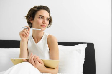 Günlüğe yazan, not defteri ve kalem tutan, düşünmeyi bir kenara bırakan, uyandıktan sonra yatakta oturan genç ve güzel bir kadının portresi..