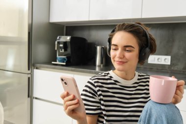 Genç kız öğrencinin portresini kapat, çay iç ve kulaklıkla müzik dinle, mutfakta akıllı telefon kullan..