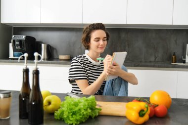 Güzel, modern bir kadının portresi, sebzelerle yemek pişiren, elinde not defteri olan, yemek tarifi yazan, not alan, yemek planları yapan, haftalarca yemek listesi yapan, mutfakta oturan bir kız..