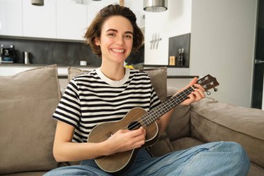 Kanepede ukulele çalan, en sevdiği şarkıyı söyleyen, küçük gitarda akor çalan, oturma odasında oturan güzel bir kız..