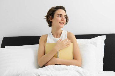 Düşüncesiz genç bir kadının portresi sabahları günlüğünü yazıyor, uyanıyor ve notlar alıyor, yatakta oturuyor, gülümsüyor ve dışarı bakıyor..