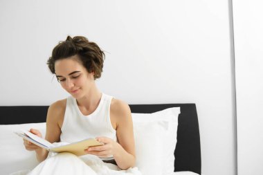 Yatakta kadın portresi, günlük tutma, defter okuma ve gülümseme..