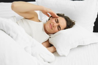 Kadın kendini iyi hissetmiyor, yatağa uzanıyor, başını okşuyor ve kaşlarını çatıyor, baş ağrısı ve şiddetli migreni var. Sağlık ve refah kavramı