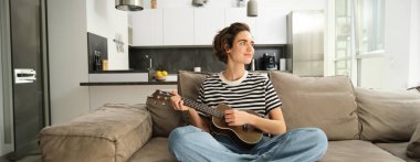 Oturma odasında dinlenen, ukulele çalan bir kızın portresi, yeni bir müzik aleti çalmayı, evde dinlenmeyi öğreniyor..