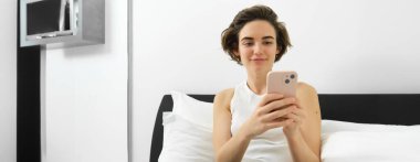 Modern bir kadın tasviri, yatakta dizüstü bilgisayarla ve akıllı telefonla dinleniyor, mesaj gönderiyor, cep telefonundan bildirimi okuyor..