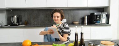 Mutfakta gülümseyen esmer kadın, haftanın yemek listesini yazıyor, yemek tarifi okuyor, salata pişiriyor, evde sebze yiyor. Yaşam tarzı kavramı