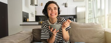 Kablosuz kulaklıkla televizyon izleyen, ilgi ve heyecanla ekrana bakan, tahıl gevreğini kasede yiyen, kaşık tutan, oturma odasındaki koltukta oturan bir kadının portresi..