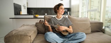 Oturma odasında dinlenen, ukulele çalan bir kızın portresi, yeni bir müzik aleti çalmayı, evde dinlenmeyi öğreniyor..