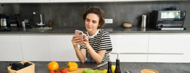 Mutfakta güzel esmer kadın portresi, yemek pişirme, akıllı telefon tarifi arama, yemek blogu için fotoğraf çekme, sebzelerden yemek pişirme, vejetaryen salatası..